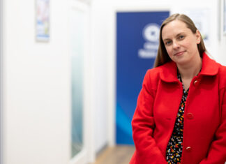 Community spirited Elise Apolloni, a community spirited pharmacist, standing in a pharmacy hallway wearing a red coat
