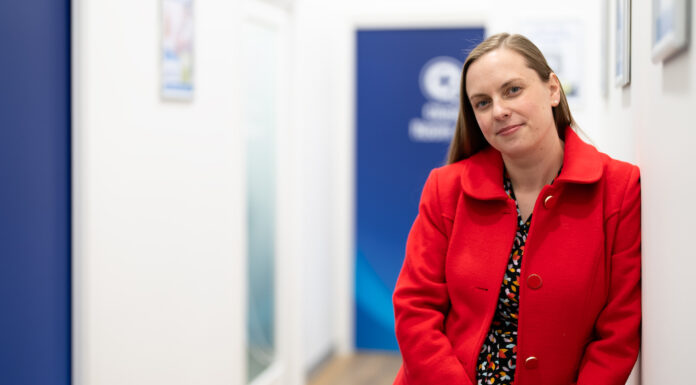 Community spirited Elise Apolloni, a community spirited pharmacist, standing in a pharmacy hallway wearing a red coat