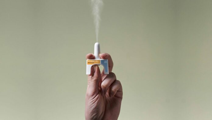 nyxoid-and-hand_cropped-2 Hand holding a naloxone nasal spray device releasing medication