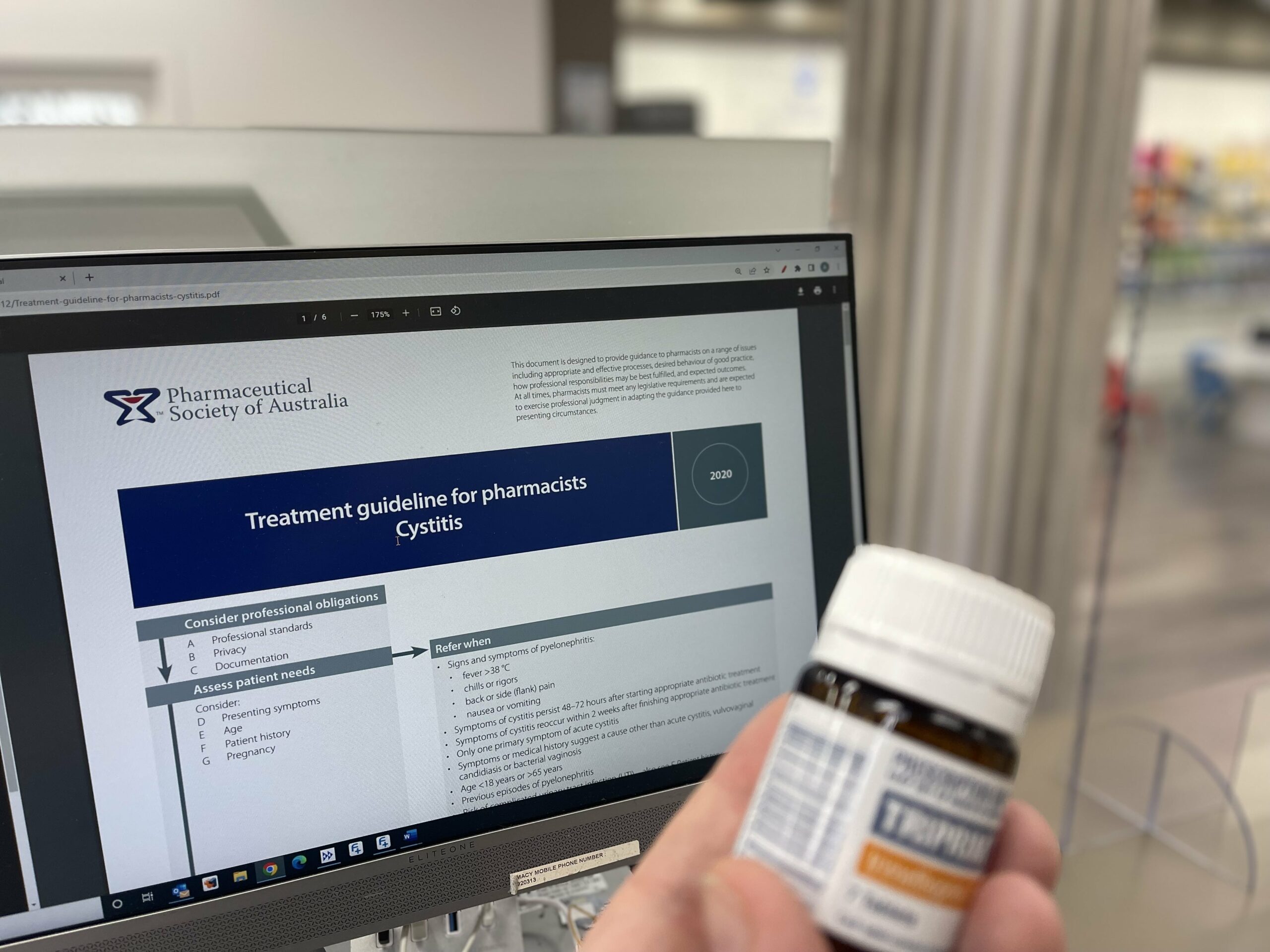 Computer screen displaying treatment guidelines for pharmacists on cystitis, with a hand holding a medication bottle