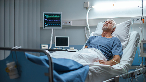 Elderly man resting in a hospital bed with monitoring equipment nearby