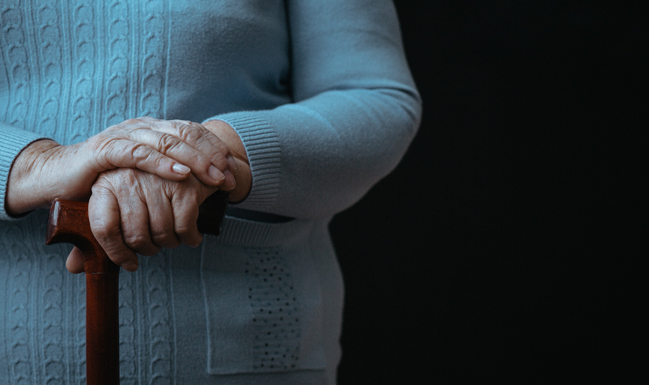 aged person resting hands on walking stick