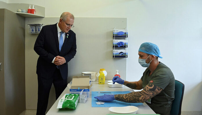Prime Minister Scott Morrison looks on as pharmacist Branko Radojkovic prepares a simulation of the COVID-19 vaccine at Sydney's Royal Prince Alfred Hospital last week